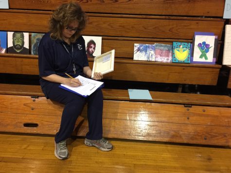 Art Teacher and art judge, Ms. Stokes, goes through some of the painting submissions in the Art contest.